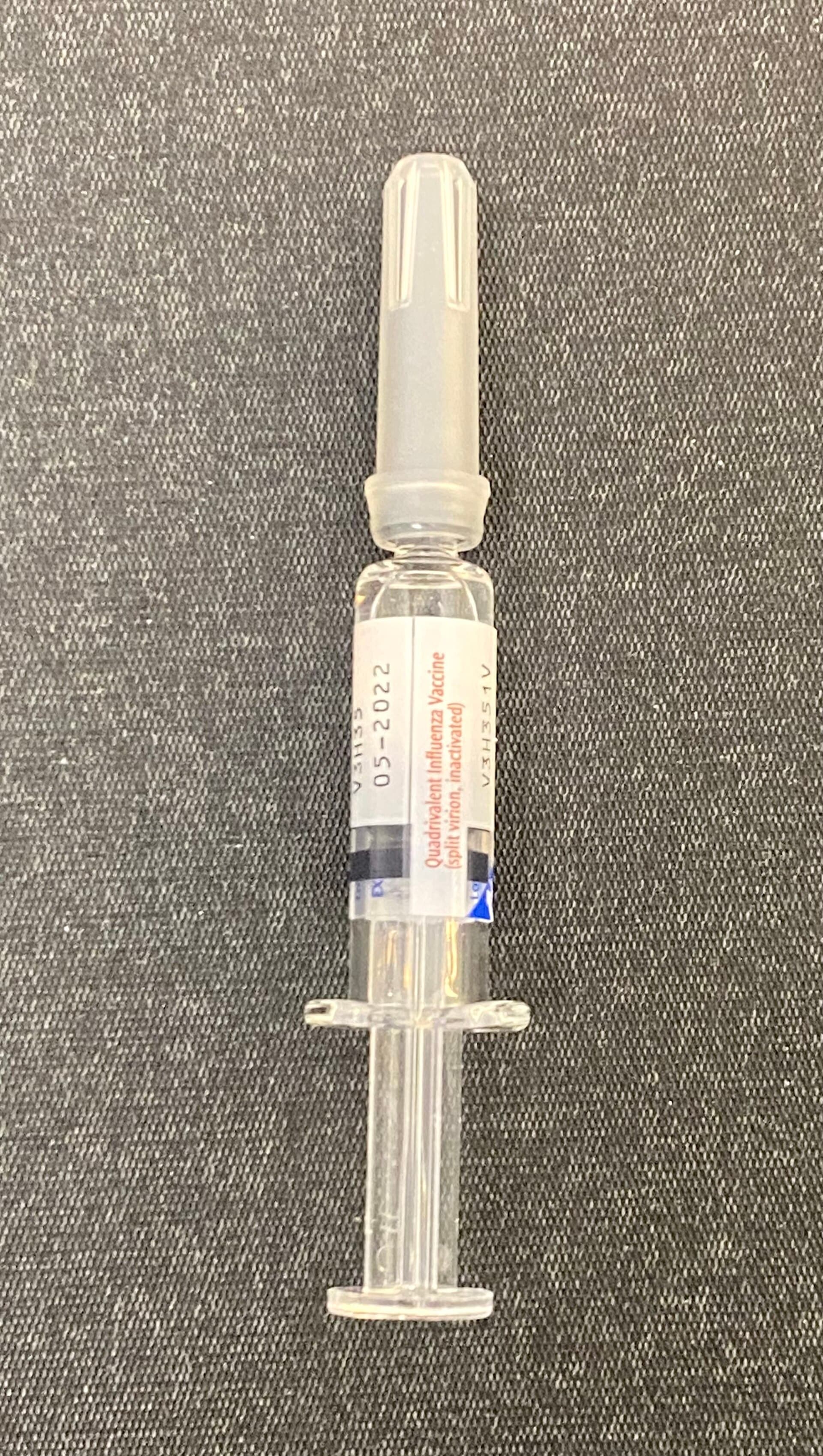 Seringa com vacina quadrivalente contra influenza sobre superfície azul